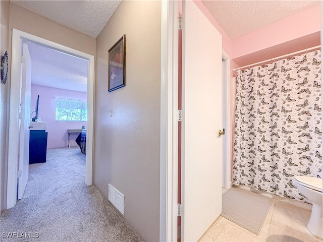 hall with visible vents, a textured ceiling, and carpet flooring