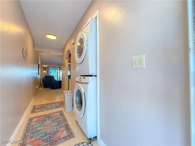 washroom with stacked washer / drying machine, baseboards, a textured ceiling, and laundry area