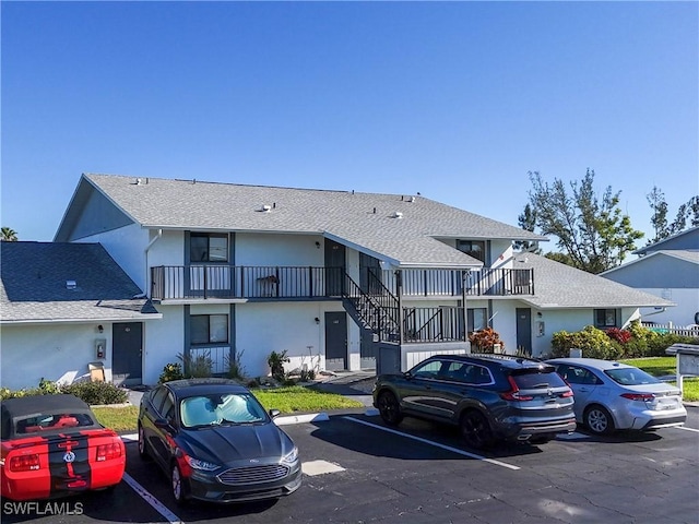 exterior space with stairway, stucco siding, roof with shingles, and uncovered parking