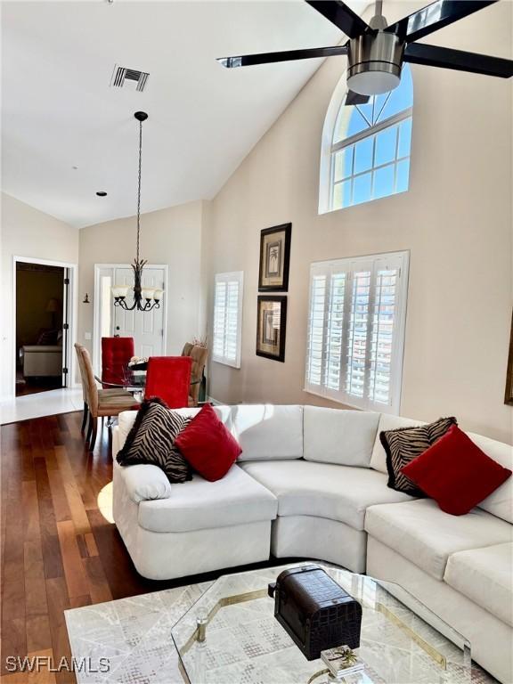 living room featuring visible vents, a healthy amount of sunlight, dark wood-style flooring, and ceiling fan with notable chandelier