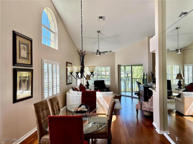 dining space featuring visible vents, ceiling fan with notable chandelier, dark wood-style flooring, and a towering ceiling