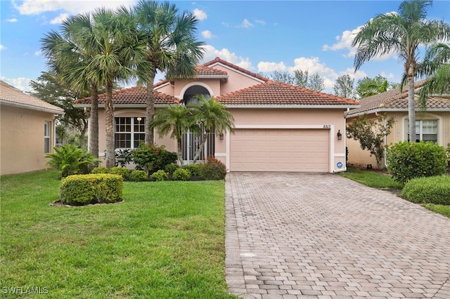 mediterranean / spanish house featuring a front lawn, a tiled roof, stucco siding, decorative driveway, and an attached garage