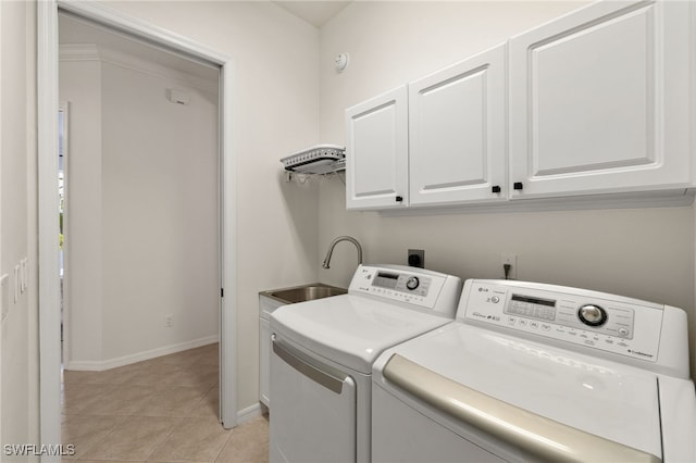 laundry area featuring a sink, cabinet space, light tile patterned floors, baseboards, and washing machine and clothes dryer