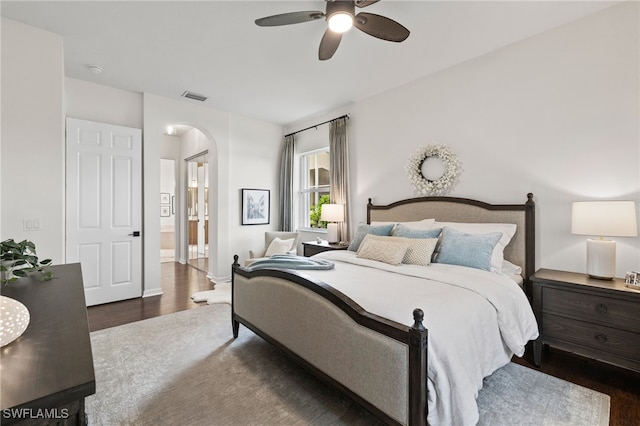 bedroom featuring visible vents, wood finished floors, arched walkways, ensuite bath, and a ceiling fan