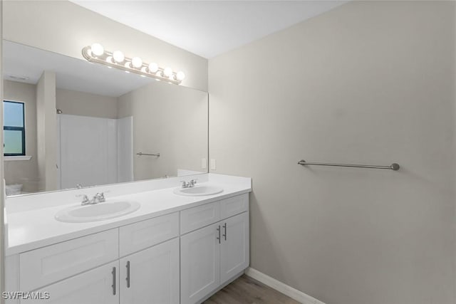 full bath featuring double vanity, wood finished floors, baseboards, and a sink