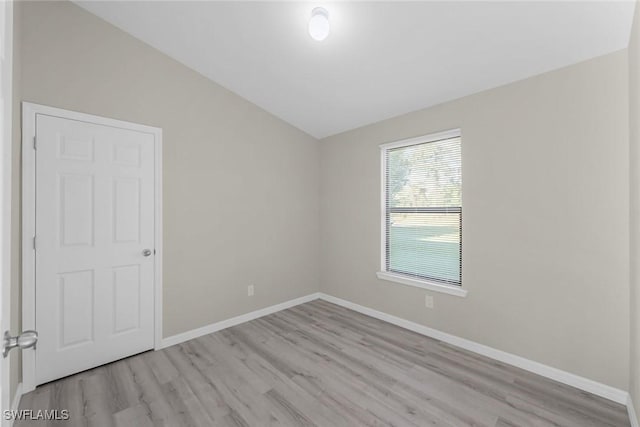 unfurnished room featuring light wood-style flooring, baseboards, and vaulted ceiling