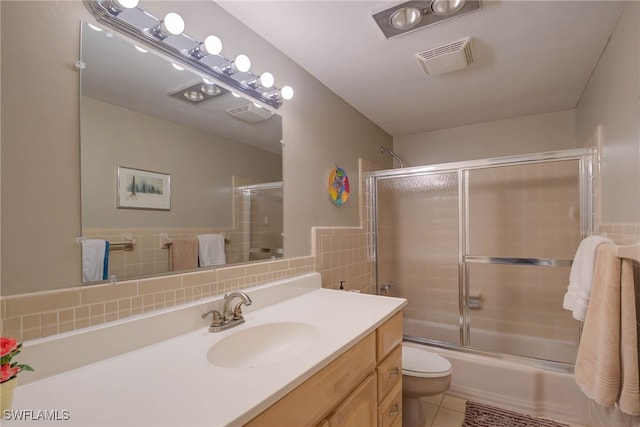 bathroom featuring vanity, visible vents, bath / shower combo with glass door, tile walls, and toilet