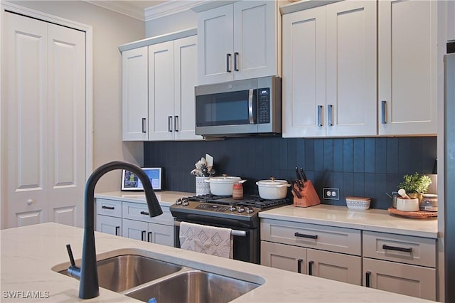 kitchen featuring light stone countertops, a sink, decorative backsplash, appliances with stainless steel finishes, and crown molding