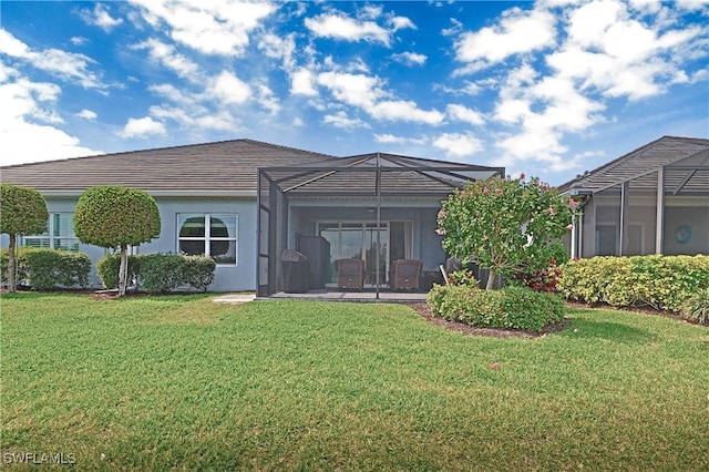 rear view of house with glass enclosure, a yard, and stucco siding