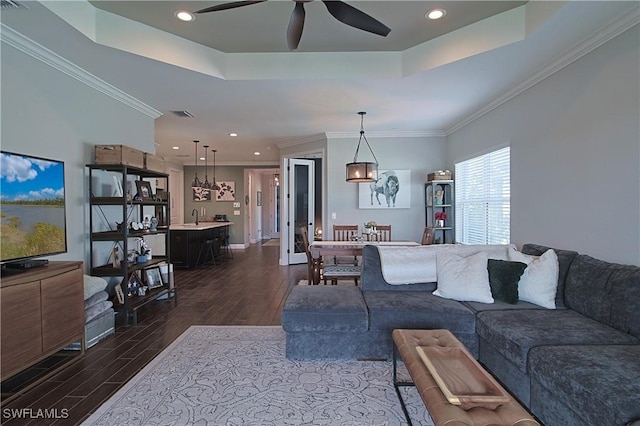 living area with ceiling fan, a tray ceiling, dark wood finished floors, and ornamental molding