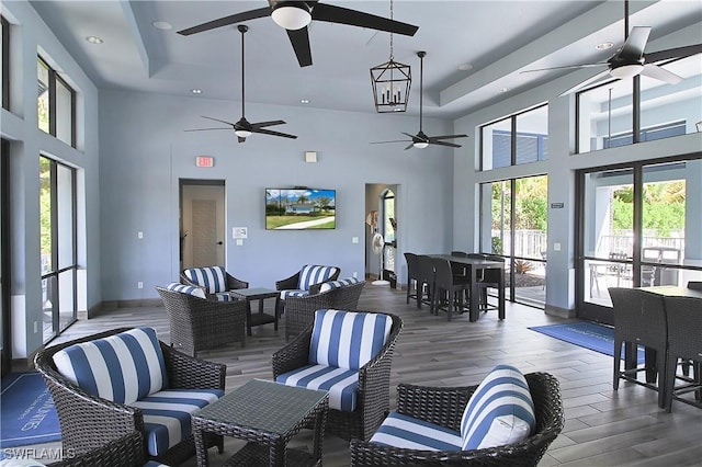 living area with wood finished floors, baseboards, a tray ceiling, a high ceiling, and recessed lighting