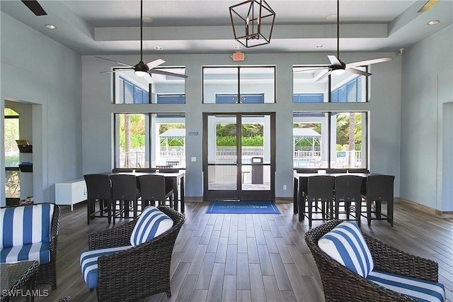 interior space featuring wood finished floors, baseboards, a tray ceiling, a high ceiling, and ceiling fan