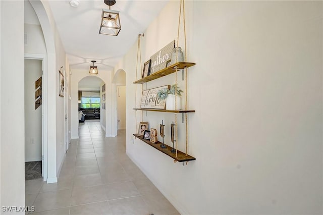 hallway with light tile patterned floors, baseboards, and arched walkways