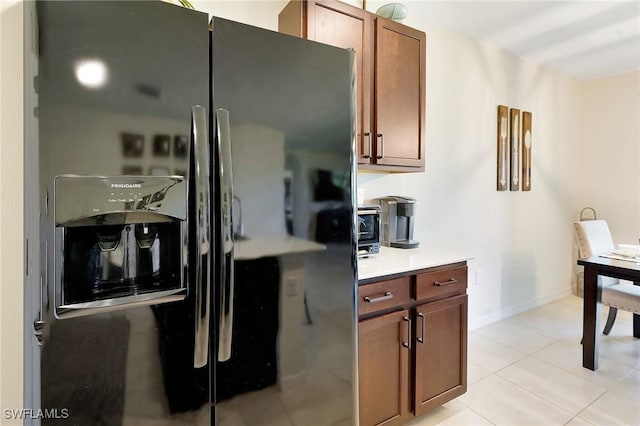 kitchen with baseboards, light countertops, light tile patterned floors, brown cabinetry, and black fridge with ice dispenser