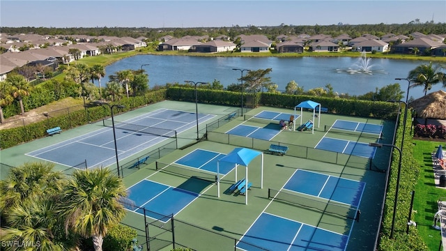 view of tennis court with a residential view, a water view, and fence