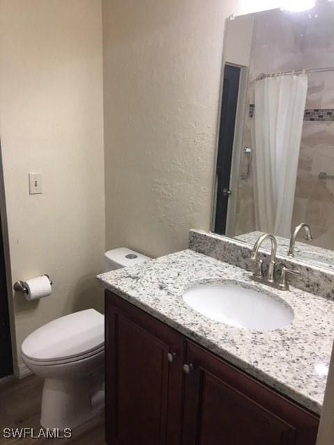 full bathroom featuring a shower with shower curtain, toilet, vanity, and a textured wall