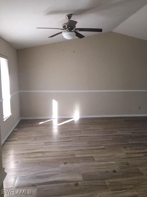 empty room featuring ceiling fan, baseboards, wood finished floors, and vaulted ceiling