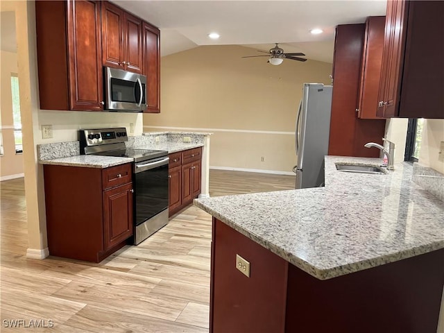 kitchen with a sink, reddish brown cabinets, appliances with stainless steel finishes, and vaulted ceiling