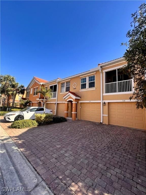 view of property with a tile roof, decorative driveway, an attached garage, and stucco siding