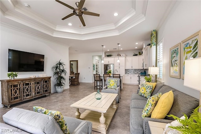 living room featuring a tray ceiling, recessed lighting, crown molding, baseboards, and ceiling fan