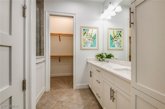 bathroom with a walk in closet, baseboards, double vanity, tile patterned floors, and a sink