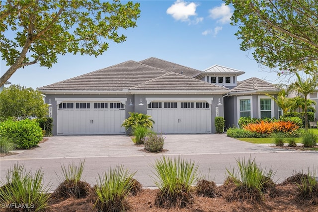 view of front of property featuring a garage, a tile roof, driveway, and stucco siding