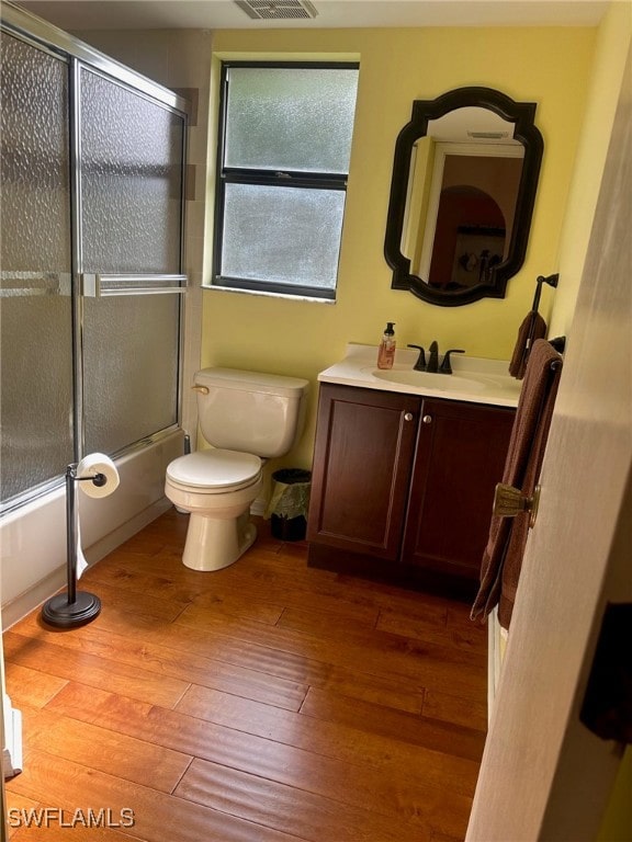 full bathroom with vanity, visible vents, shower / bath combination with glass door, hardwood / wood-style flooring, and toilet