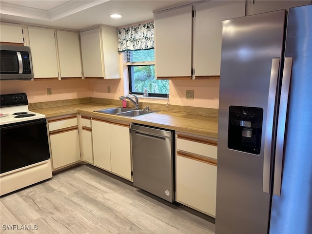 kitchen with light wood finished floors, a sink, ornamental molding, light countertops, and stainless steel appliances