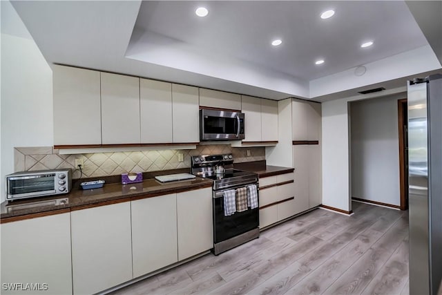 kitchen featuring dark countertops, light wood finished floors, a toaster, decorative backsplash, and appliances with stainless steel finishes