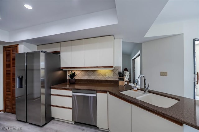 kitchen with backsplash, dark stone counters, stainless steel appliances, white cabinetry, and a sink