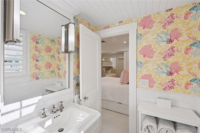 ensuite bathroom featuring a sink, wainscoting, ensuite bathroom, and wallpapered walls