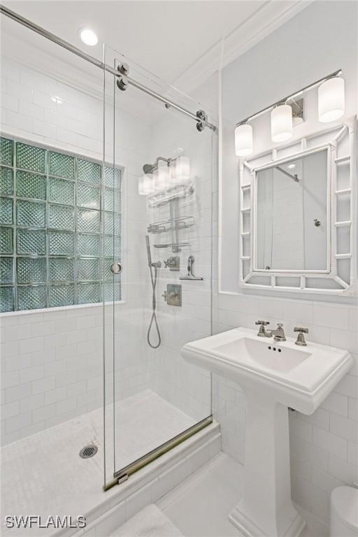 full bathroom with a shower stall, crown molding, tile walls, and a sink