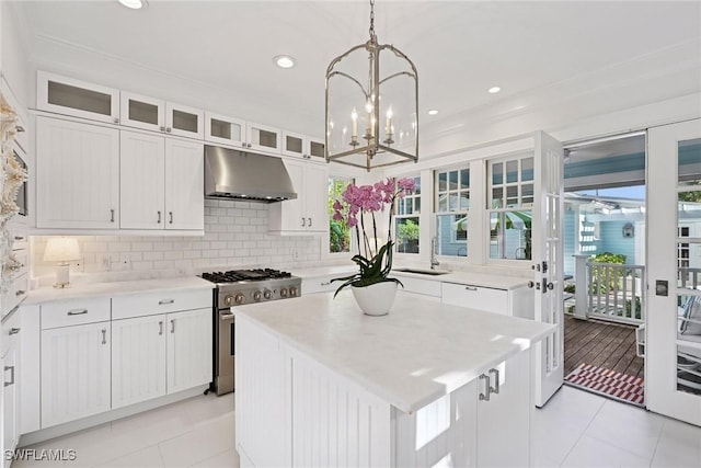 kitchen with under cabinet range hood, white cabinetry, tasteful backsplash, and stainless steel range