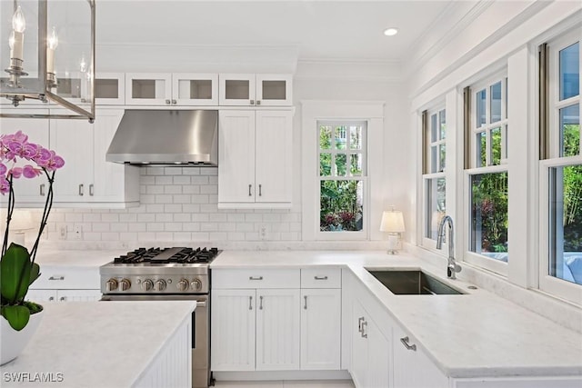 kitchen featuring under cabinet range hood, decorative backsplash, high end stainless steel range oven, white cabinets, and a sink