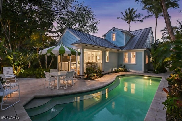 pool at dusk with a patio and an outdoor pool