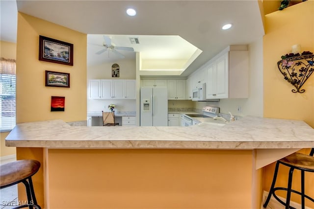 kitchen with visible vents, white appliances, a peninsula, a breakfast bar area, and light countertops