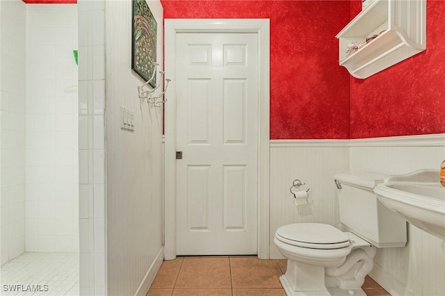 full bathroom with tile patterned floors, tiled shower, wainscoting, and toilet