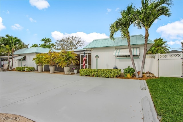 view of front of house with glass enclosure, a front yard, a gate, fence, and metal roof