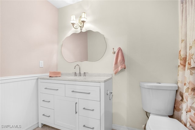 bathroom featuring vanity, toilet, and a wainscoted wall