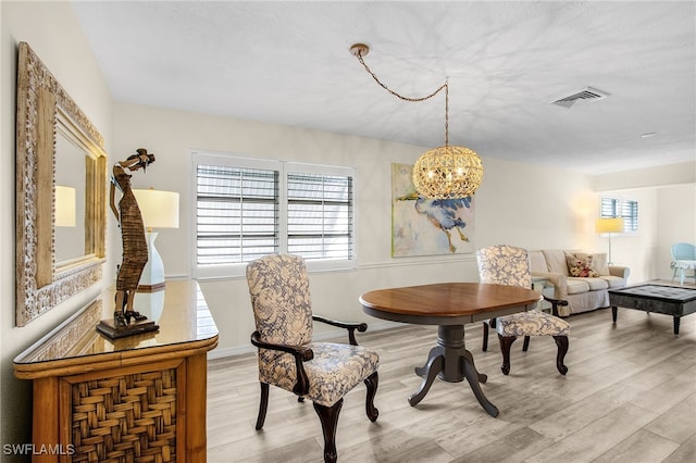 dining space with light wood-type flooring, baseboards, an inviting chandelier, and visible vents