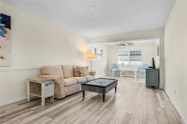 living area with baseboards, light wood-type flooring, and ceiling fan