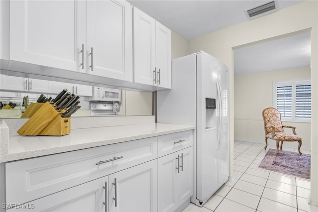 kitchen with visible vents, light stone counters, white fridge with ice dispenser, white cabinets, and light tile patterned floors