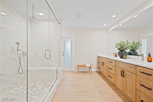 bathroom with a sink, a marble finish shower, wood finished floors, and double vanity