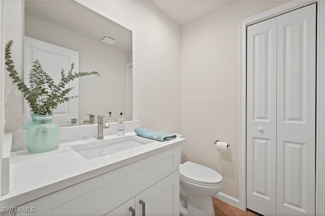 half bath with vanity, wood finished floors, visible vents, a closet, and toilet