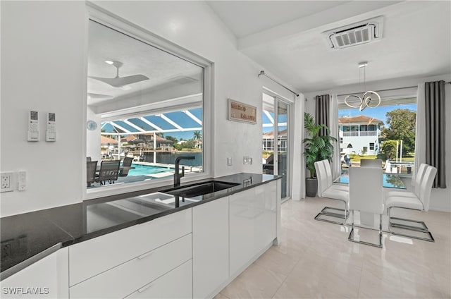 kitchen featuring visible vents, a sink, pendant lighting, white cabinetry, and dark countertops