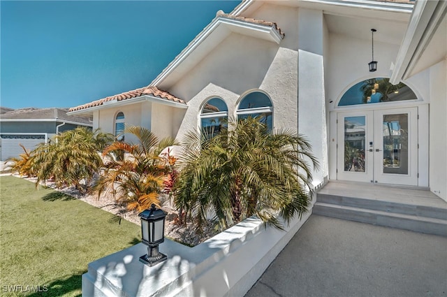 entrance to property with french doors, a yard, an attached garage, and stucco siding