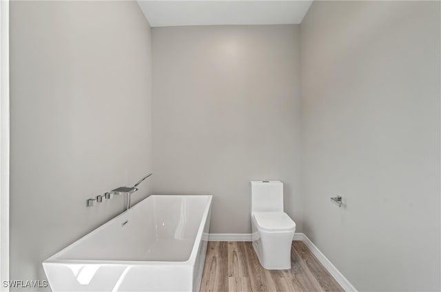 bathroom featuring wood finished floors, a freestanding tub, baseboards, and toilet