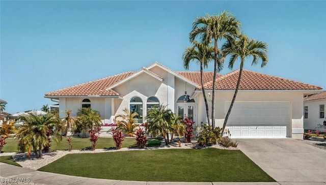mediterranean / spanish-style home featuring driveway, a front yard, a garage, stucco siding, and a tiled roof