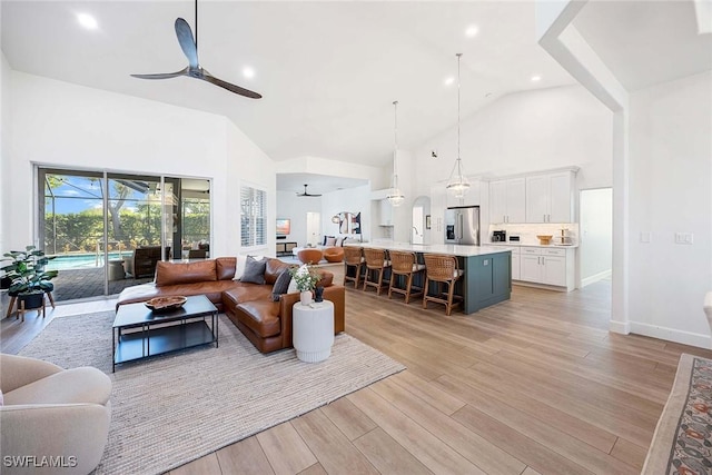 living area with high vaulted ceiling, a ceiling fan, recessed lighting, light wood-style floors, and baseboards