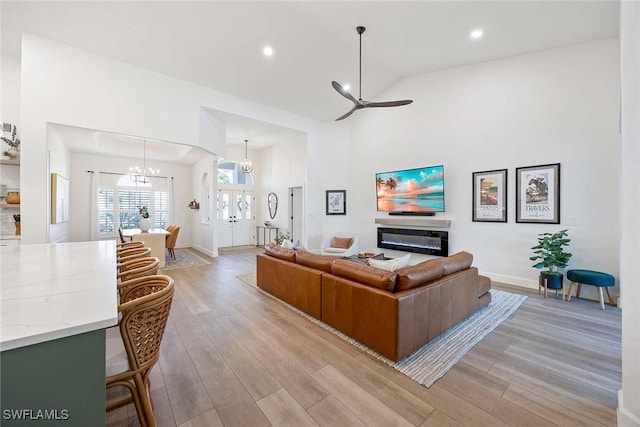 living room featuring light wood finished floors, ceiling fan with notable chandelier, a high ceiling, and baseboards